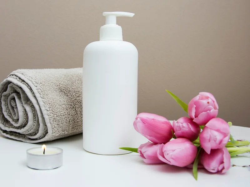 Khăn bông cuộn, chai dầu dưỡng, nến nhỏ và bó tulip hồng